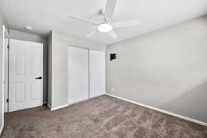 Unfurnished bedroom featuring a closet, a textured ceiling, a ceiling fan, and dark carpet