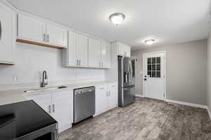 Kitchen with stainless steel appliances, white cabinets, light wood finished floors, and light stone counters