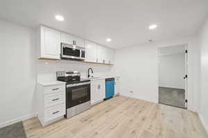 Kitchen featuring stainless steel appliances, white cabinets, light wood-type flooring, backsplash, and recessed lighting