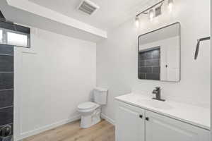 Full bathroom with vanity, light wood-style floors, and a textured ceiling