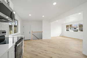 Kitchen with stainless steel appliances, light wood-style flooring, white cabinets, recessed lighting, and light stone countertops