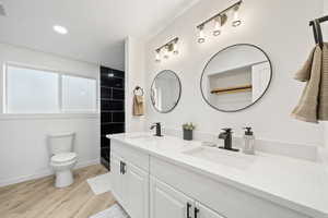 Bathroom featuring double vanity, light wood-type flooring, and tiled shower