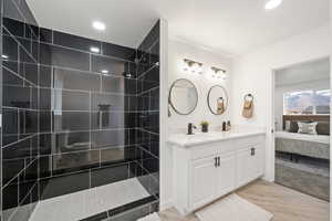 Ensuite bathroom featuring double vanity, walk in shower, light wood finished floors, and a textured ceiling