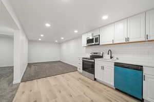Kitchen featuring white cabinets, stainless steel appliances, light wood-style floors, recessed lighting, and backsplash