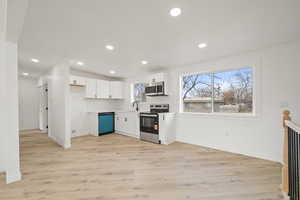 Kitchen featuring light countertops, stainless steel appliances, light wood-style flooring, white cabinets, and decorative backsplash