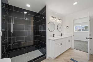 Full bath with double vanity, walk in shower, light wood-type flooring, and recessed lighting