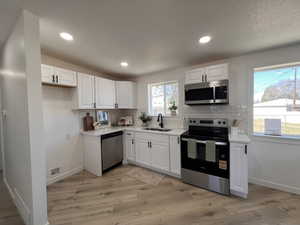 Kitchen with stainless steel appliances, white cabinetry, light wood-type flooring, tasteful backsplash, and recessed lighting