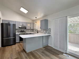 Kitchen featuring gray cabinetry, lofted ceiling, decorative light fixtures, stainless steel appliances, and a peninsula