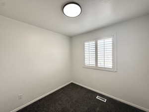 Empty room with dark colored carpet and a textured ceiling