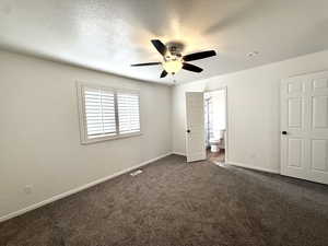 Unfurnished bedroom with dark colored carpet, a textured ceiling, ensuite bathroom, and a ceiling fan