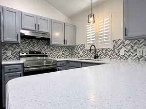 Kitchen with gray cabinets, stainless steel electric range, lofted ceiling, pendant lighting, and decorative backsplash