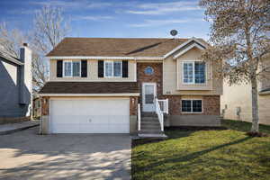 Bi-level home featuring brick siding, concrete driveway, a front lawn, and an attached garage