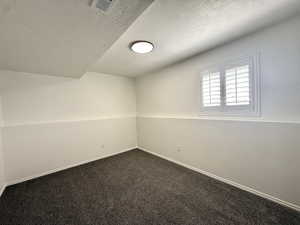 Empty room featuring a textured ceiling and dark colored carpet