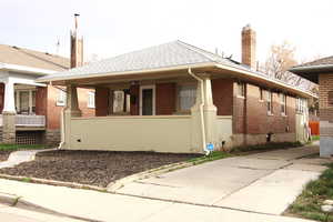 View of property exterior with brick siding, a chimney, covered porch, and a shingled roof