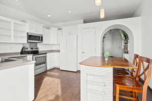 Kitchen featuring arched walkways, stainless steel appliances, open shelves, light wood-type flooring, and white cabinetry