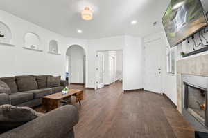 Living room with arched walkways, a tiled fireplace, dark wood finished floors, and recessed lighting