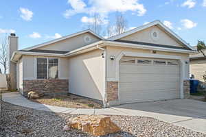 View of front of property with stone siding, an attached garage, a chimney, and concrete driveway