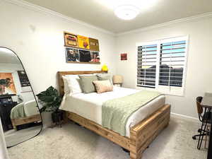 Bedroom with ornamental molding, light carpet, and plantation shutters