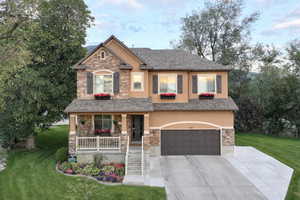 Craftsman house featuring a covered porch, stone and stucco siding, large driveway, and mature trees