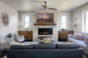 Living area featuring a stone fireplace, a wainscoted wall, ceiling fan, and hardwood floors
