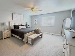 Spacious master bedroom with light carpet, plantation shutters, and ceiling fan