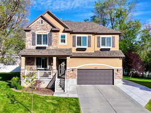 Craftsman-style house with stone siding, a porch, a front lawn, and stucco siding