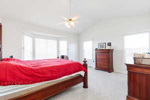 Bedroom featuring light colored carpet, multiple windows, ceiling fan, and lofted ceiling