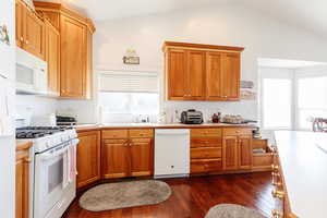 Kitchen featuring white appliances, light countertops, dark wood finished floors, wood finish cabinetry, and lofted ceiling
