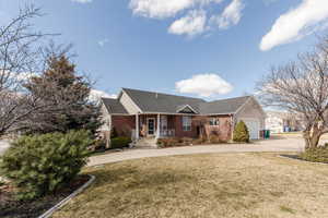 Single story home featuring a porch, a front yard, brick siding, a garage, and driveway
