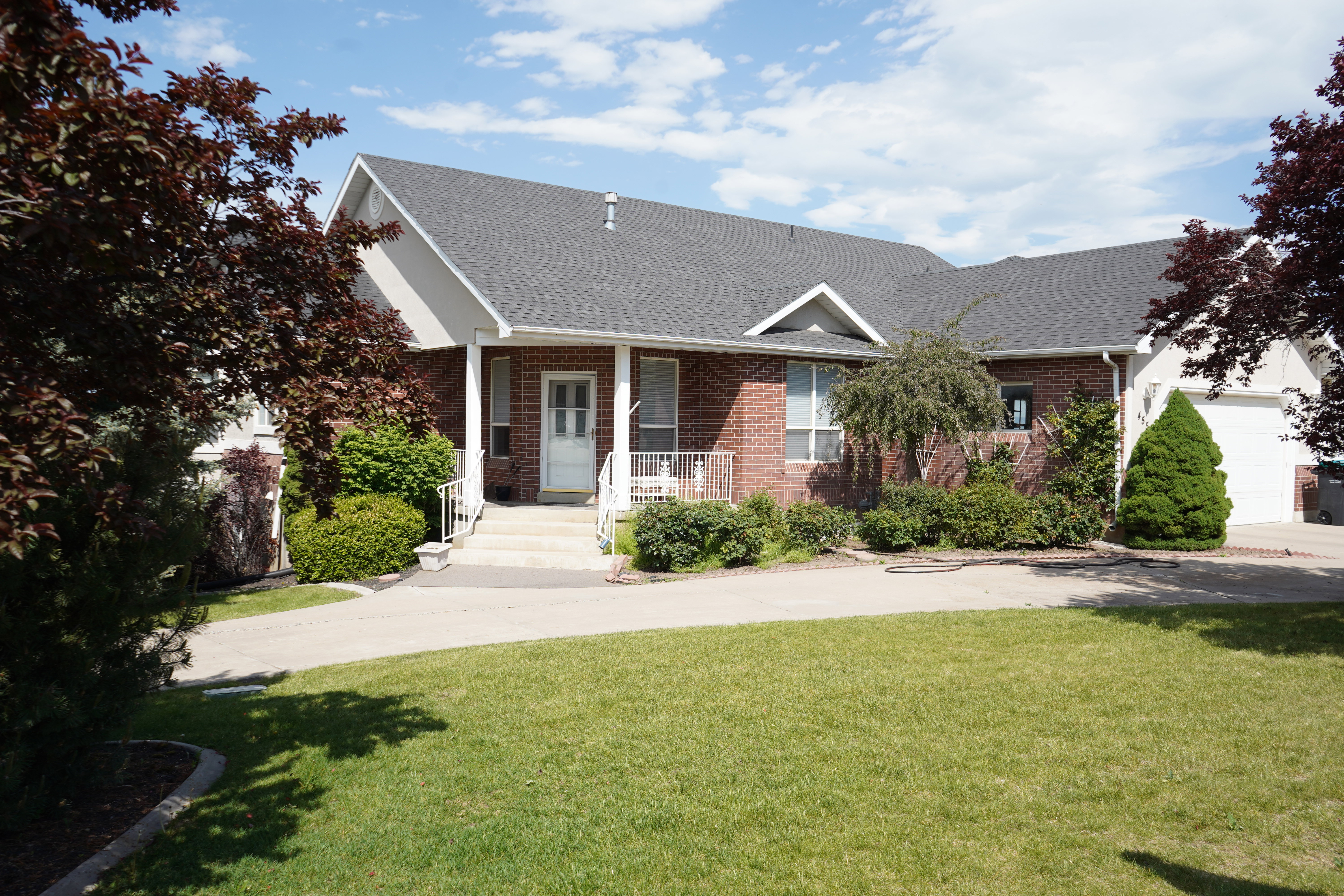 Brick exterior with white trim, a covered porch, a concrete driveway, a two-car garage, and established landscaping
