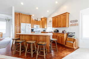 Kitchen featuring white appliances, arched walkways, light countertops, a breakfast bar, and dark wood finished floors