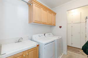 Laundry room featuring ornamental molding, cabinet space, and washer and clothes dryer