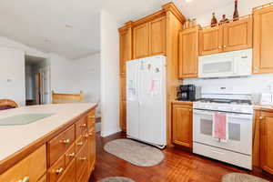 Kitchen featuring white appliances, light countertops, dark wood finished floors, vaulted ceiling, and wood finish cabinetry