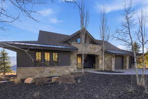 View of front of home with stone siding, a garage, covered porch, board and batten siding, and roof with shingles