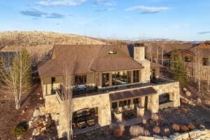 Back of house featuring a patio, a chimney, outdoor dining area, a shingled roof, and stone siding