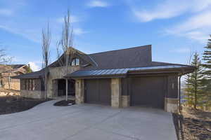 View of front of home with stone siding, a standing seam roof, concrete driveway, an attached garage, and a shingled roof