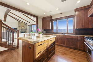 Kitchen with vaulted ceiling with beams, high end range, a center island, light wood-type flooring, and healthy amount of natural light