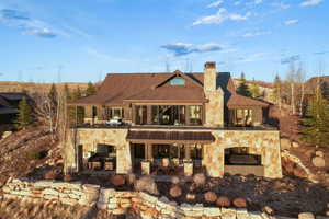 Rear view of property featuring stone siding, a chimney, a patio area, and a shingled roof