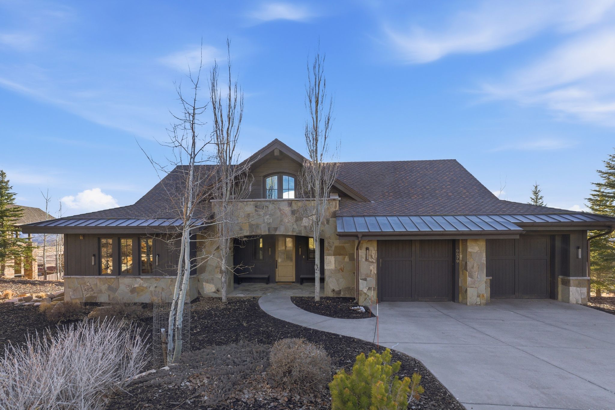 View of front of house featuring stone siding, a standing seam roof, driveway, a garage, and a shingled roof