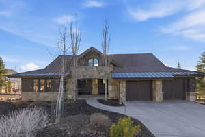 View of front of house featuring stone siding, a standing seam roof, driveway, a garage, and a shingled roof