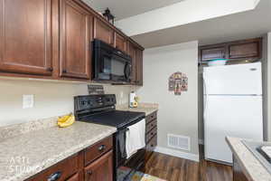 Kitchen with black appliances, light countertops, dark wood-type flooring, and dark wood finish cabinetry