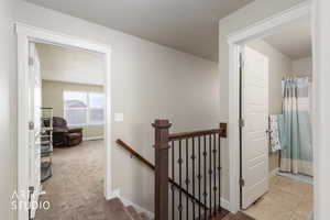Hallway with an upstairs landing and light colored carpet