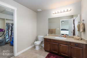 Ensuite bathroom featuring vanity, a walk in closet, light tile patterned floors, and ceiling fan