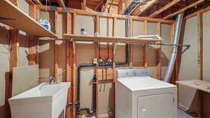 Basement laundry room featuring washer, dryer, and sink