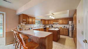 Kitchen featuring wood finish cabinets, a raised ceiling, a breakfast bar area, a peninsula, and light countertops