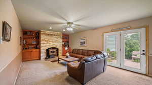 Living room featuring light carpet, a ceiling fan, built in shelves, a textured ceiling, and a wood stove