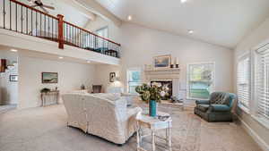 Living area with a fireplace with raised hearth, light colored carpet, recessed lighting, a ceiling fan, and vaulted ceiling