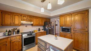 Kitchen with a kitchen island, wood finish cabinetry, stainless steel appliances, hanging light fixtures, and ornamental molding