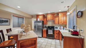 Basement Kitchen featuring wood finish cabinetry, a breakfast bar, stainless steel appliances, light tile patterned floors, and a kitchen island
