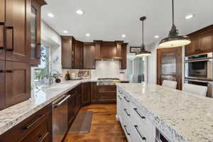 Kitchen with two tone cabinets, light stone counters, stainless steel appliances, dark wood-style floors, and pendant lighting